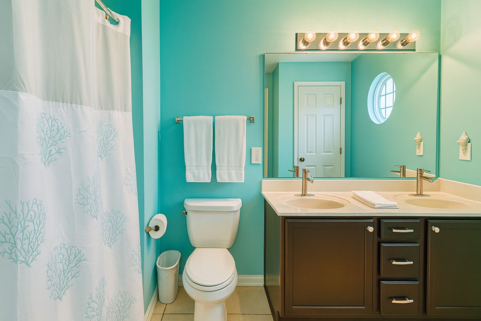 Une salle de bain équipée de toilettes, de deux lavabos, d’un miroir et d’un rideau de douche.