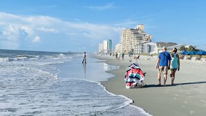 A beach with a clear sky, waves, and a few people walking. - High Tide 5 Bedroom Ocean View House, Heated Pool, Hot Tub, Darts, King beds (Surfside Beach)