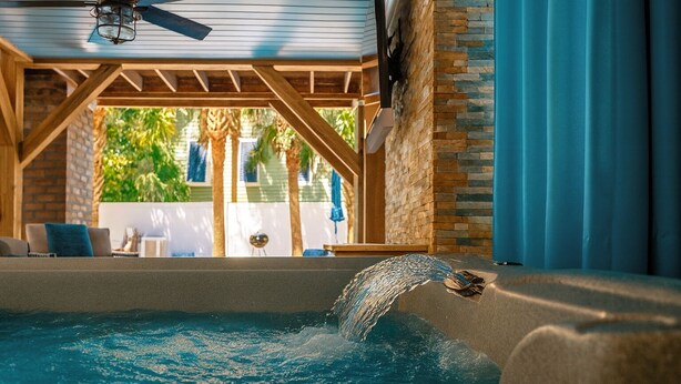 A swimming pool with a waterfall feature, surrounded by a wooden pergola and stone walls. - High Tide 5 Bedroom Ocean View House, Heated Pool, Hot Tub, Darts, King beds (Surfside Beach)