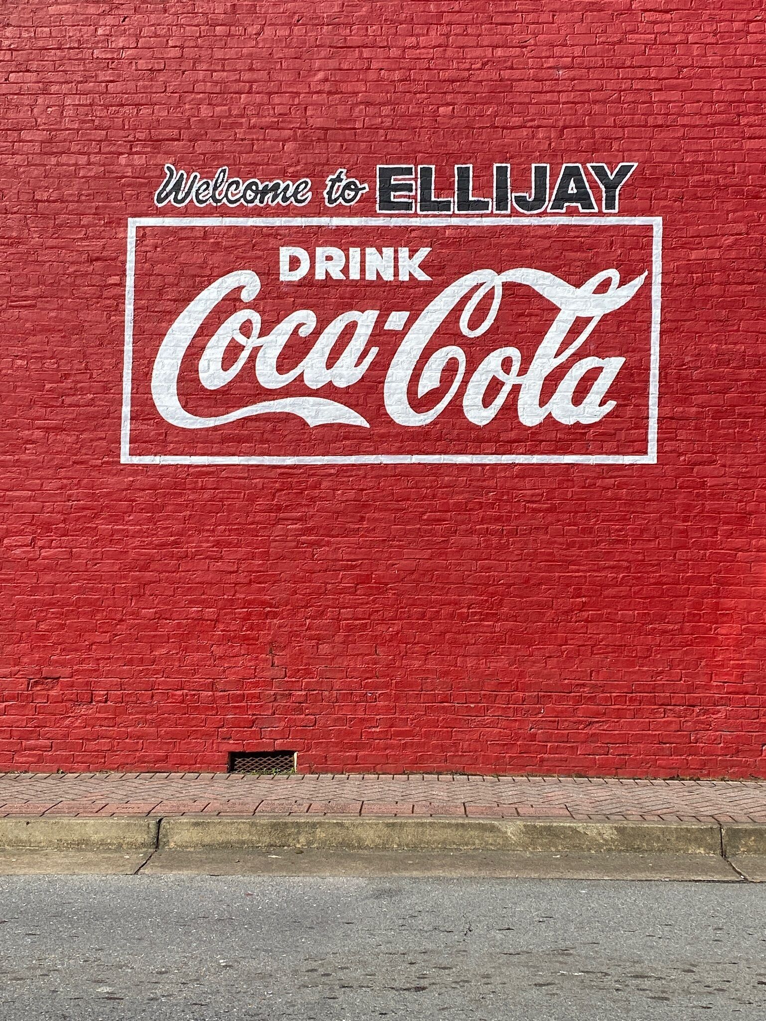 A red brick wall with a Coca-Cola sign and the text 'Welcome to ELLIJAY.'