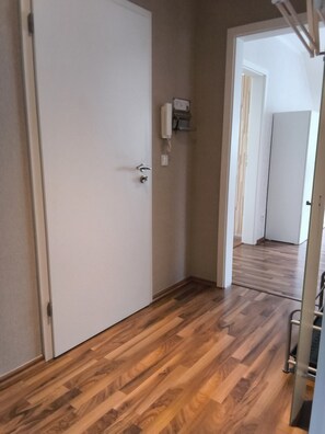 Een hal met houten vloer, een witte deur en een lichtschakelaar aan de muur.