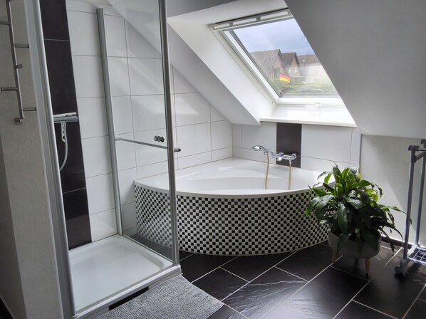 A modern bathroom with a skylight, a bathtub, a shower, and a potted plant.