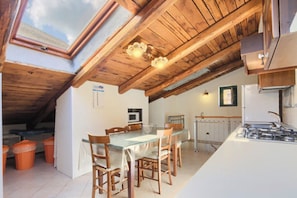 A kitchen with a wooden ceiling, a dining table with chairs, a stove, and a window with a view of the sky.