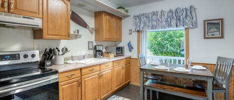 A kitchen with wooden cabinets, a stove, a microwave, and a dining area with a table and chairs.