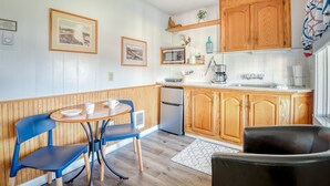 A compact kitchen with wooden cabinets, a microwave, a refrigerator, and a small dining area with blue chairs. - T05 - Dinghy @ Trollers Lodge (Depoe Bay)