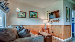 A living room with a sofa, ottoman, wooden panel walls, a TV, and framed artwork. - T05 - Dinghy @ Trollers Lodge (Depoe Bay)
