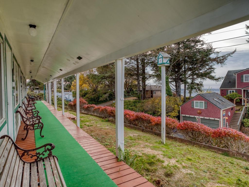 A covered outdoor area with benches, a green carpet, and a house in the background.