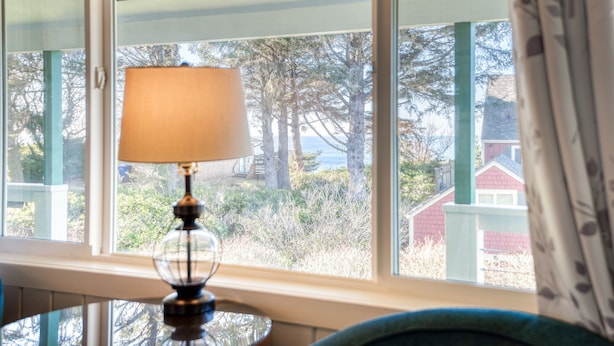 A lamp on a table by a window with a view of trees and a building. - T09 - Lighthouse @ Trollers Lodge (Depoe Bay)