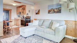 A living room with a sectional sofa, a dining area with wooden chairs, a kitchen with wooden cabinets, and a painting on the wall. - T10 - Skiff @ Trollers Lodge (Depoe Bay)