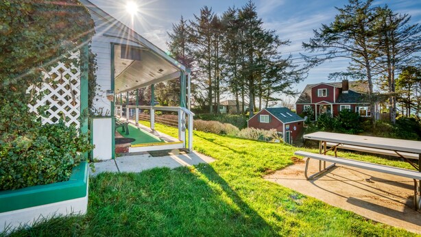 A covered outdoor area with a picnic table, a white lattice structure, and a red building in the background. - T08 - Schooner @ Trollers Lodge (Depoe Bay)