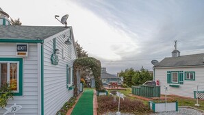 A residential area with a green pathway, white houses with green trim, and a sign indicating an exit. - T08 - Schooner @ Trollers Lodge (Depoe Bay)
