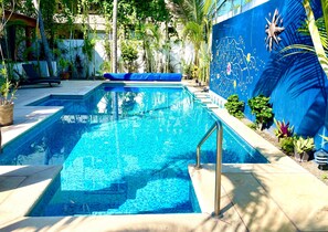 Una piscina con bordo piastrellato blu, circondata da piante in vaso e un murale sulla parete adiacente.