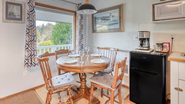 A dining area with a round wooden table, six chairs, and a black refrigerator. - T02 - Beacon @ Trollers Lodge (Depoe Bay)
