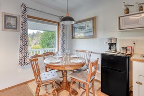 A dining area with a round wooden table, six chairs, and a black refrigerator. - T02 - Beacon @ Trollers Lodge (Depoe Bay)