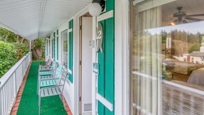 A covered porch with green chairs and a white railing, a green door with a number, and a view of a house through a window. - T02 - Beacon @ Trollers Lodge (Depoe Bay)