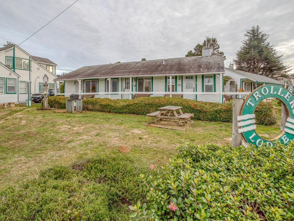 A two-story building with a green and white exterior, a picnic table in the front yard, and a sign that reads "TROLLEY LODGE".