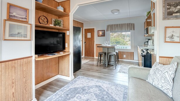Una sala de estar con televisor, muebles de madera, un sofá y una zona de comedor con taburetes.