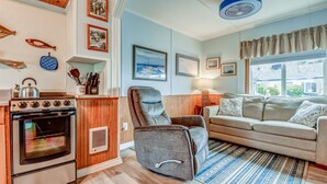 Una sala de estar acogedora con un sofá, un sillón reclinable y una zona de cocina con horno.