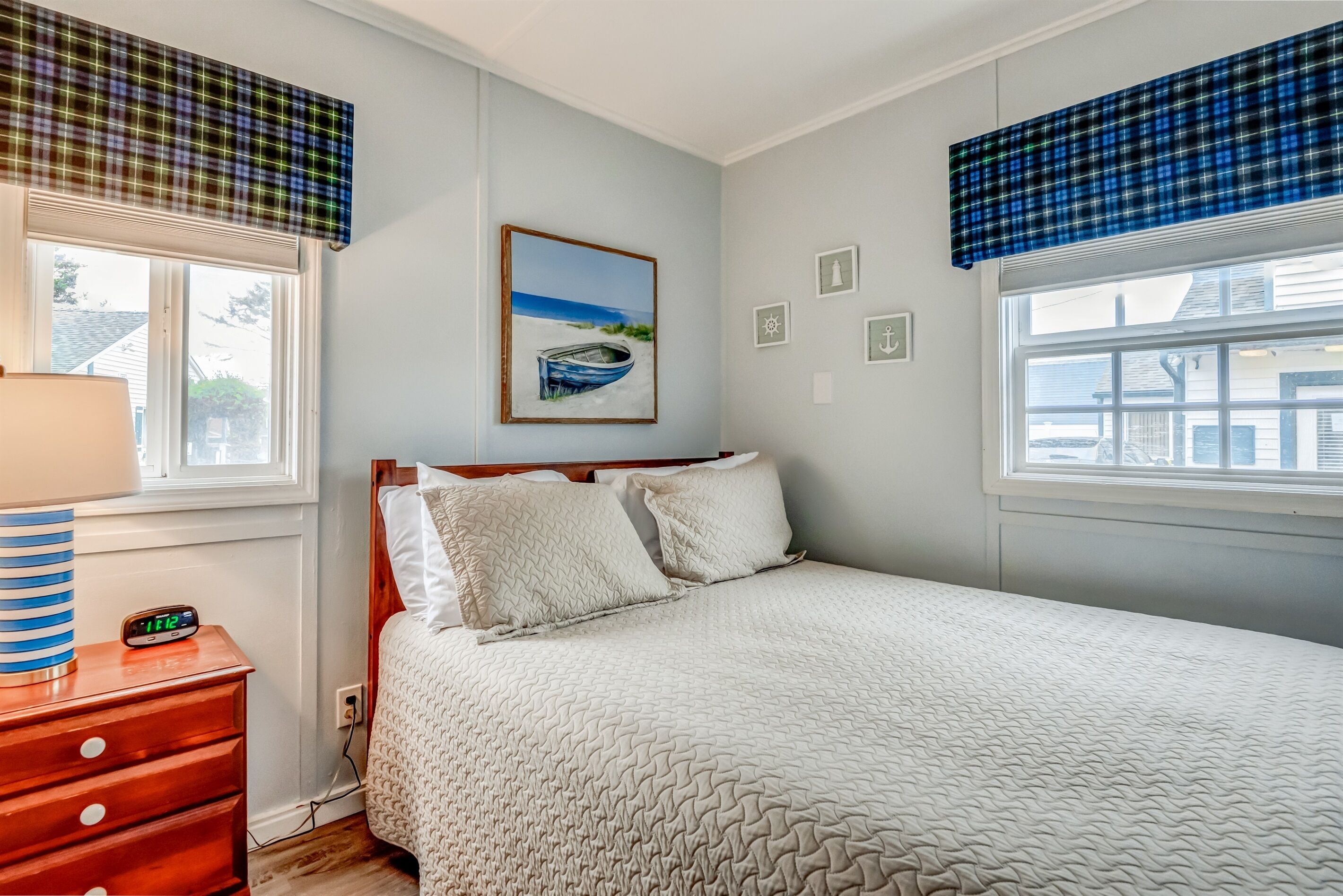 A bedroom with a bed, a nightstand, a lamp, a clock, and a painting on the wall.