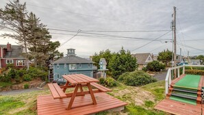 Un área de picnic con una mesa y bancos de madera, rodeada de un césped y casas residenciales.
