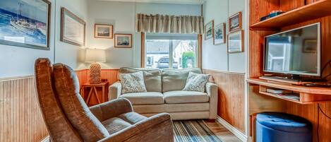 A cozy living room with a sofa, armchair, and TV stand.