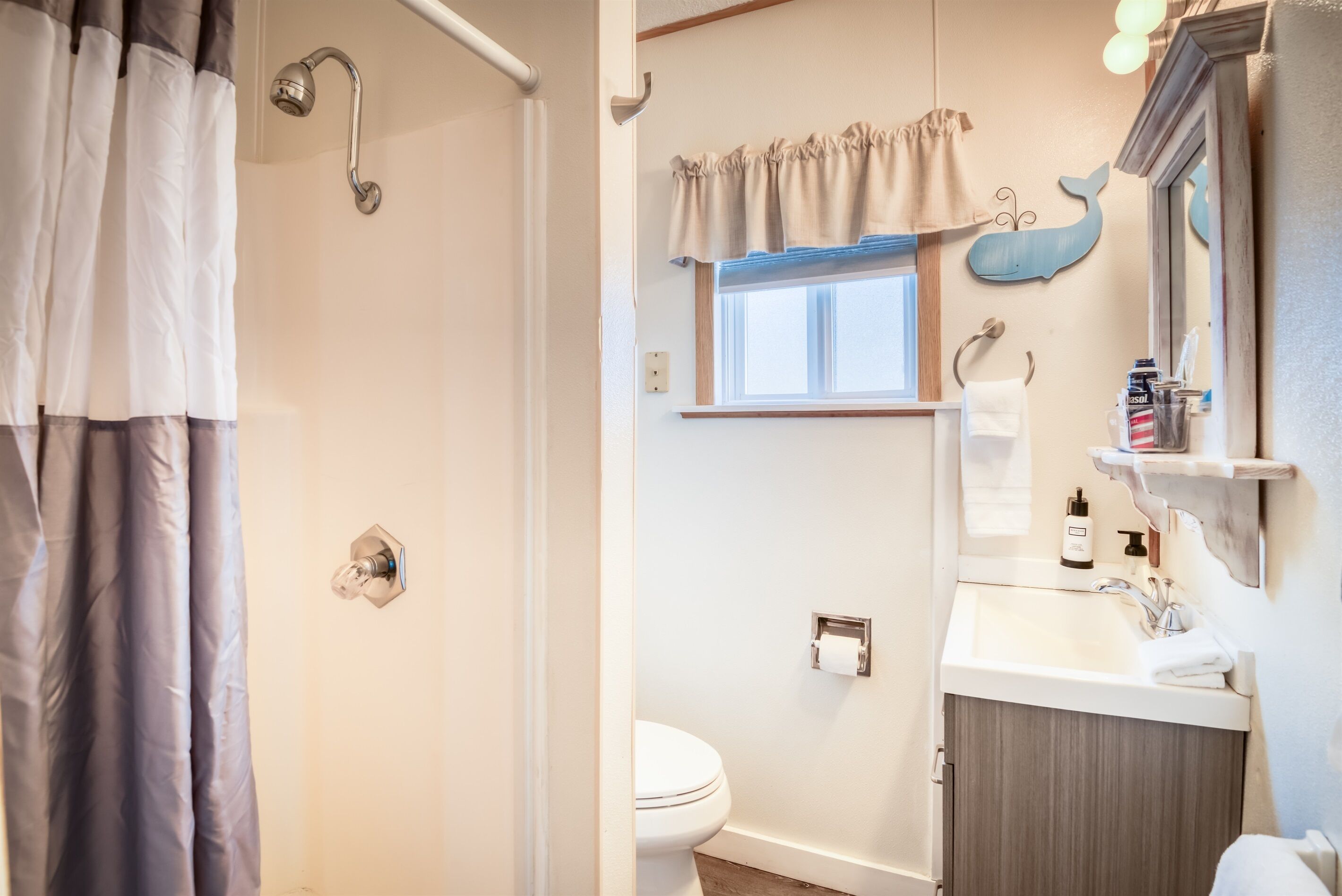 A bathroom with a shower curtain, a toilet, a sink with a mirror, and a window with a curtain.