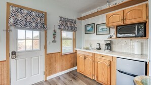 A kitchen with wooden cabinets, a microwave, a refrigerator, and a window with patterned curtains. - T06 - Dory @ Trollers Lodge (Depoe Bay)