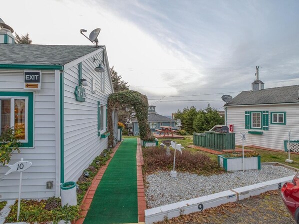 Zona residencial con un sendero verde, casas blancas con detalles verdes y un letrero que indica una salida.