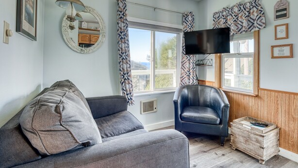 A room with a sofa, a chair, a television, a window with curtains, and a wall-mounted mirror. - T06 - Dory @ Trollers Lodge (Depoe Bay)