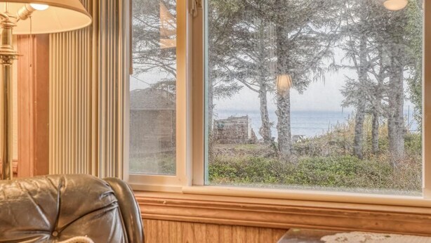 A room with a large window overlooking a forested area and a body of water. - T12 - Whaler @ Trollers Lodge (Depoe Bay)