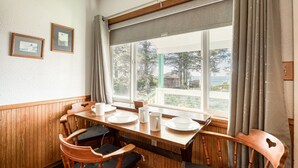 A dining area with a wooden table, chairs, and a window with curtains. - T12 - Whaler @ Trollers Lodge (Depoe Bay)