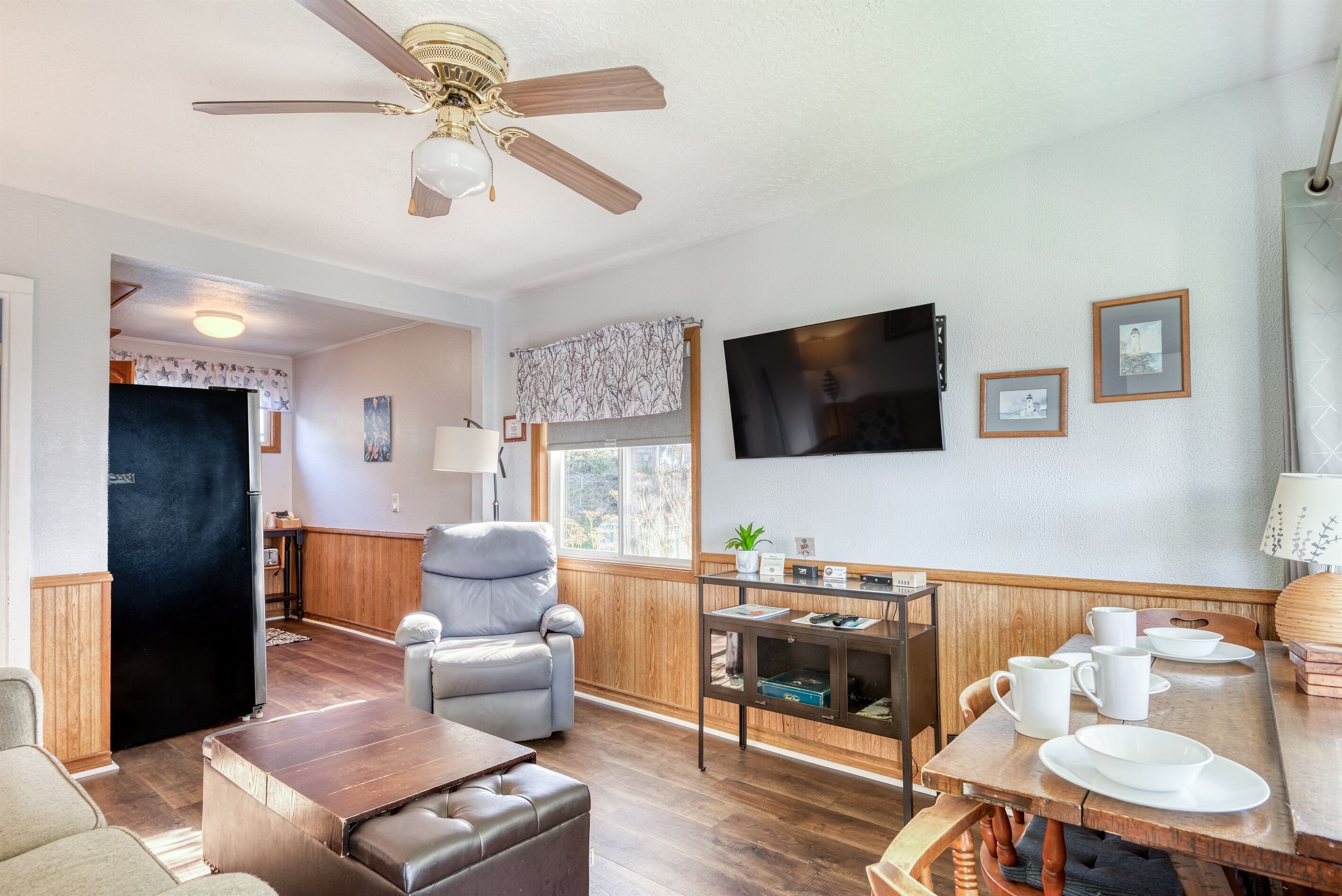 A living room with a ceiling fan, a television, a dining table with plates and cups, a sofa, and a fireplace.
