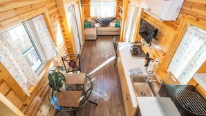 Una cabaña compacta con kitchenette, comedor y zona de estar con sofá y cojines.