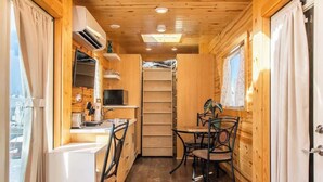 Una cabaña de madera compacta y bien iluminada con kitchenette, comedor y tragaluz.