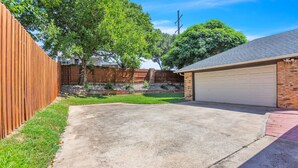 A residential backyard with a concrete driveway, a wooden fence, and a garage. - Experience Lake Views at our 4-Bedroom Home near Rowlett/Rockwall (Rowlett)