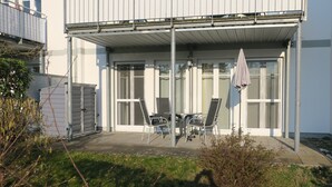 A building with a covered patio area featuring a table and chairs, a hanging umbrella, and a view of the adjacent building. - Ground floor apartment Gerbera (Zinnowitz)