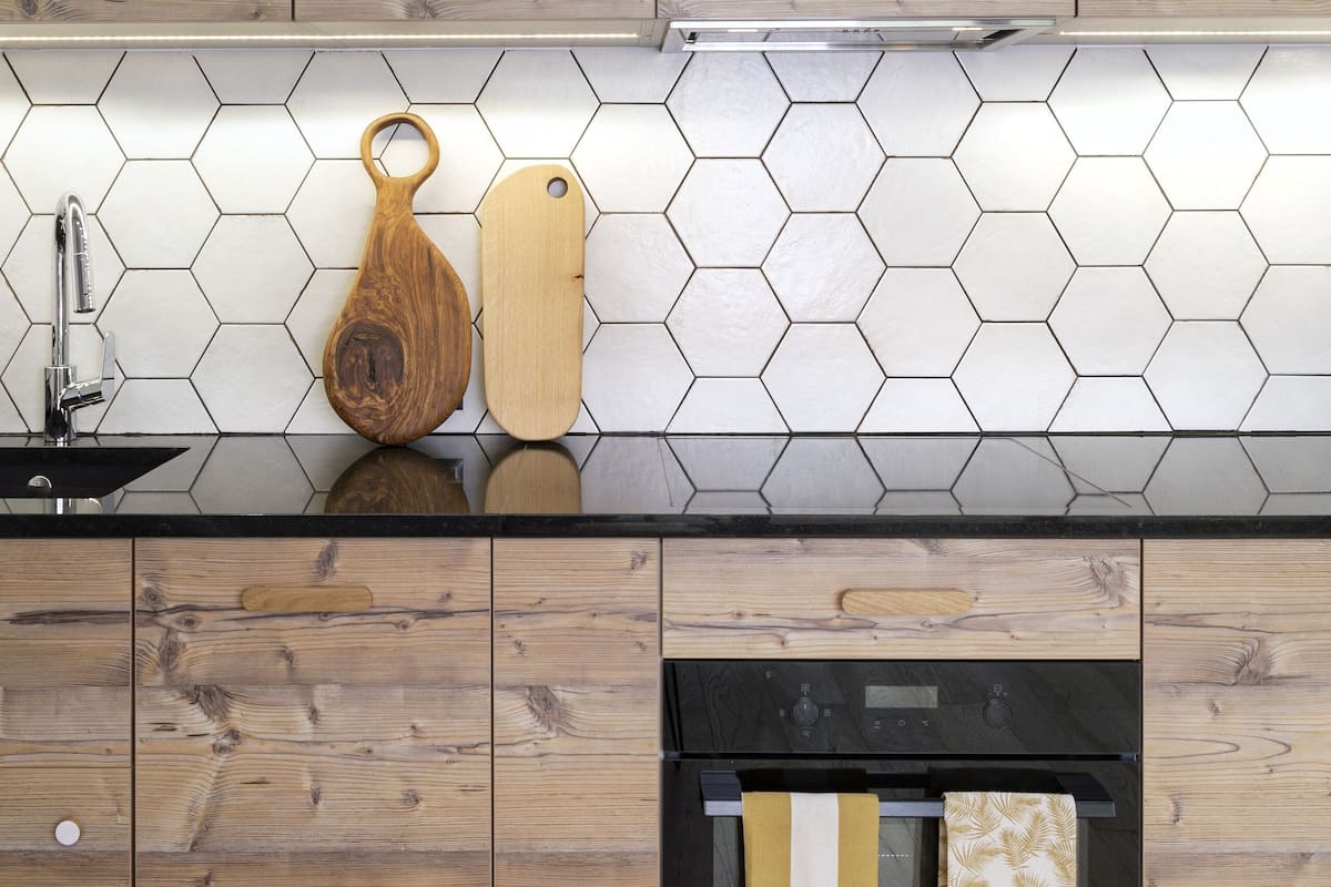A kitchen with wooden cabinets, a hexagonal tile backsplash, and a stainless steel range hood.