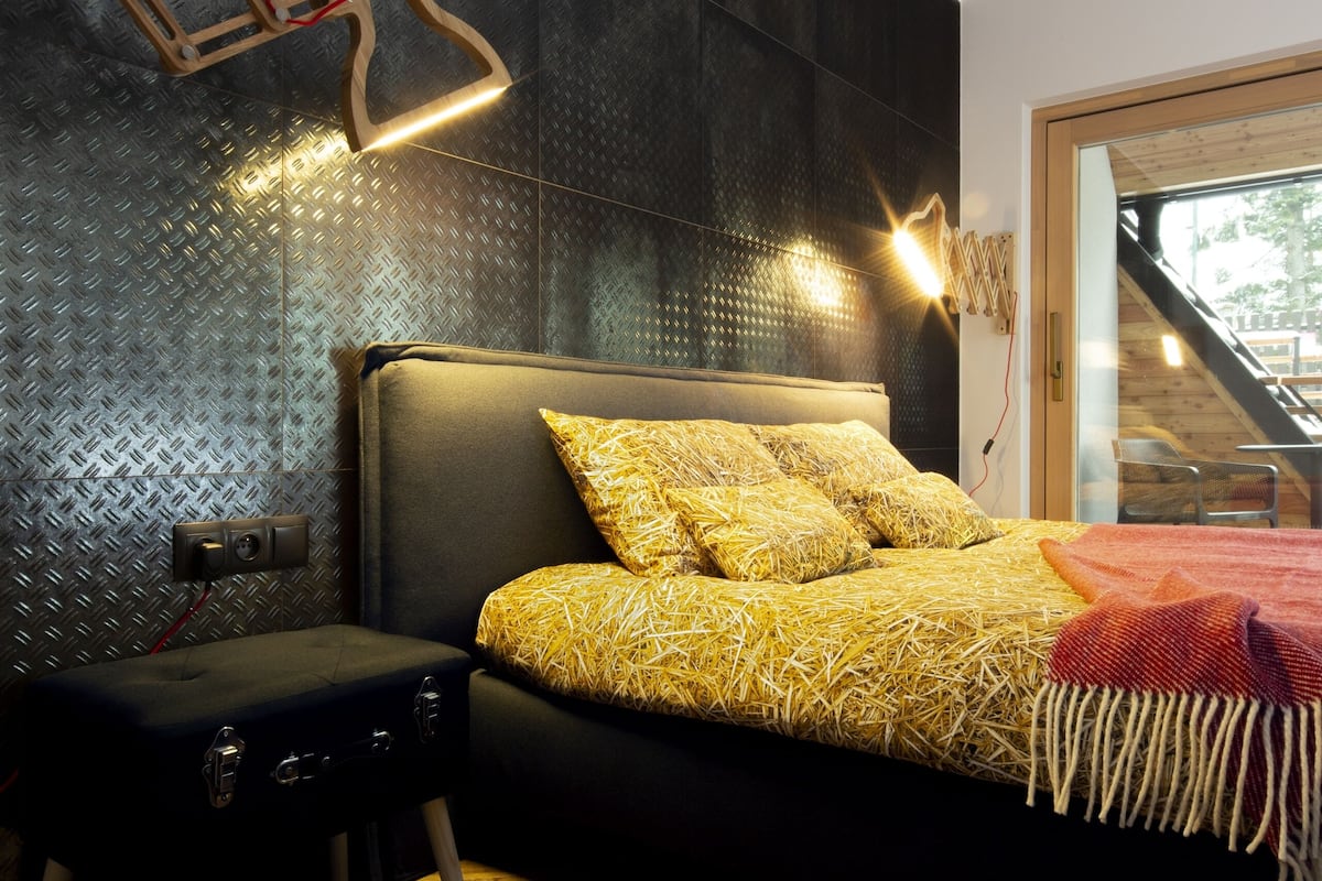 A modern bedroom with a bed, a bench, and a staircase visible through a glass door.