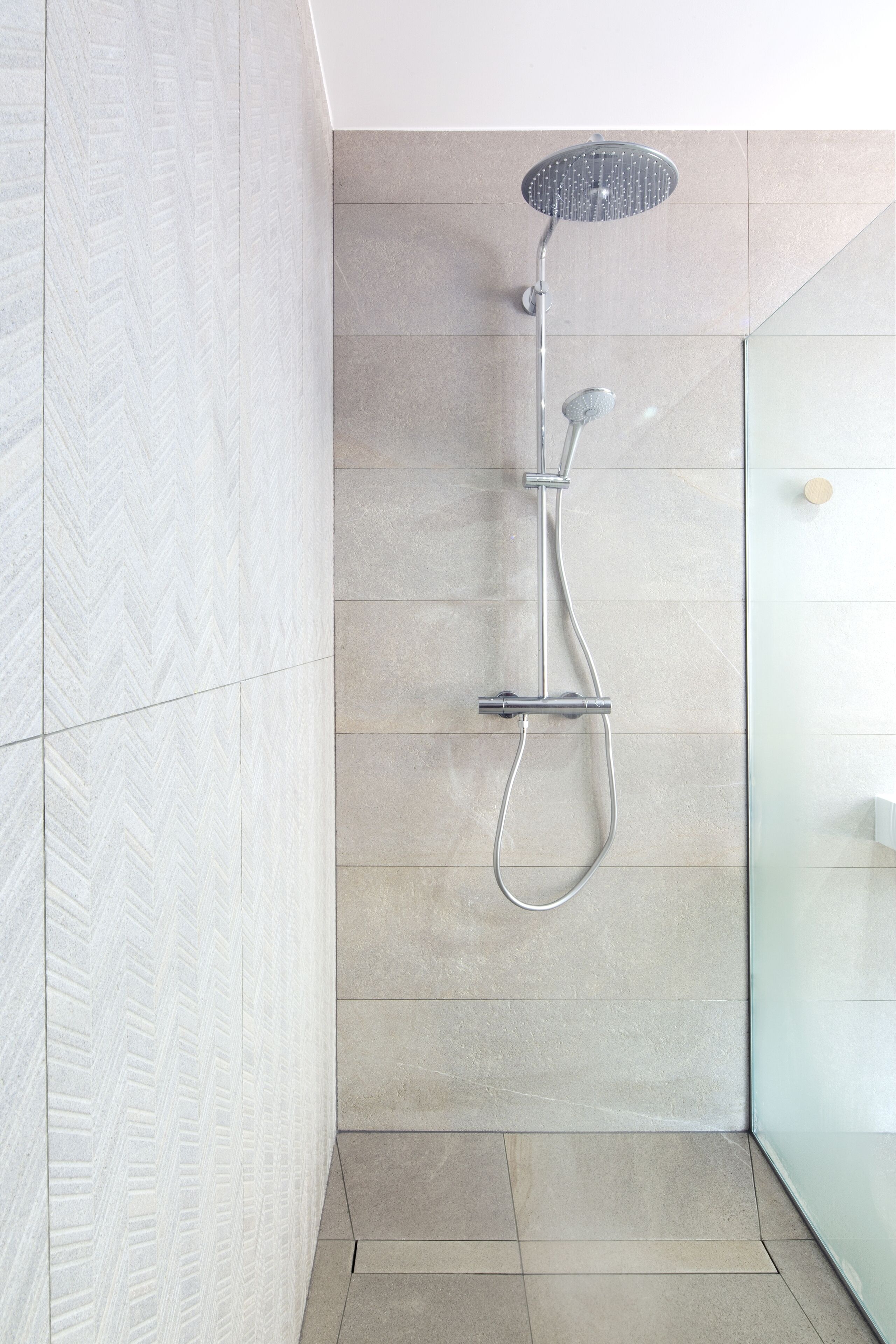 A modern shower with a handheld showerhead and a wall-mounted faucet.