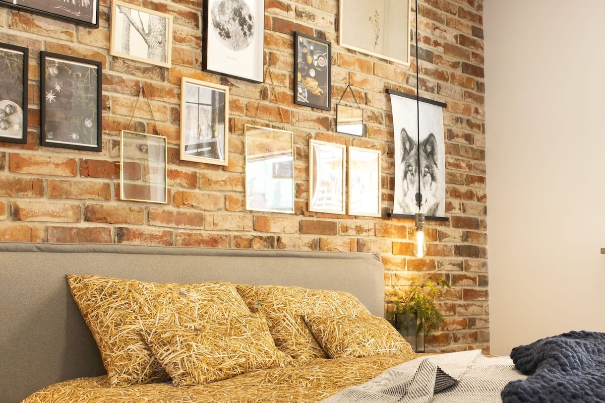 A cozy room with a brick wall, a grey sofa with straw-patterned cushions, and various framed artworks.