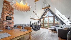 A modern living room with a brick fireplace, a hanging chair, a sofa, and a dining table. - Green Deer Premium (Zakopane)