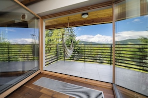 A balcony with a hammock, wooden floor, and a view of green hills and a clear sky. - Green Deer Premium (Zakopane)