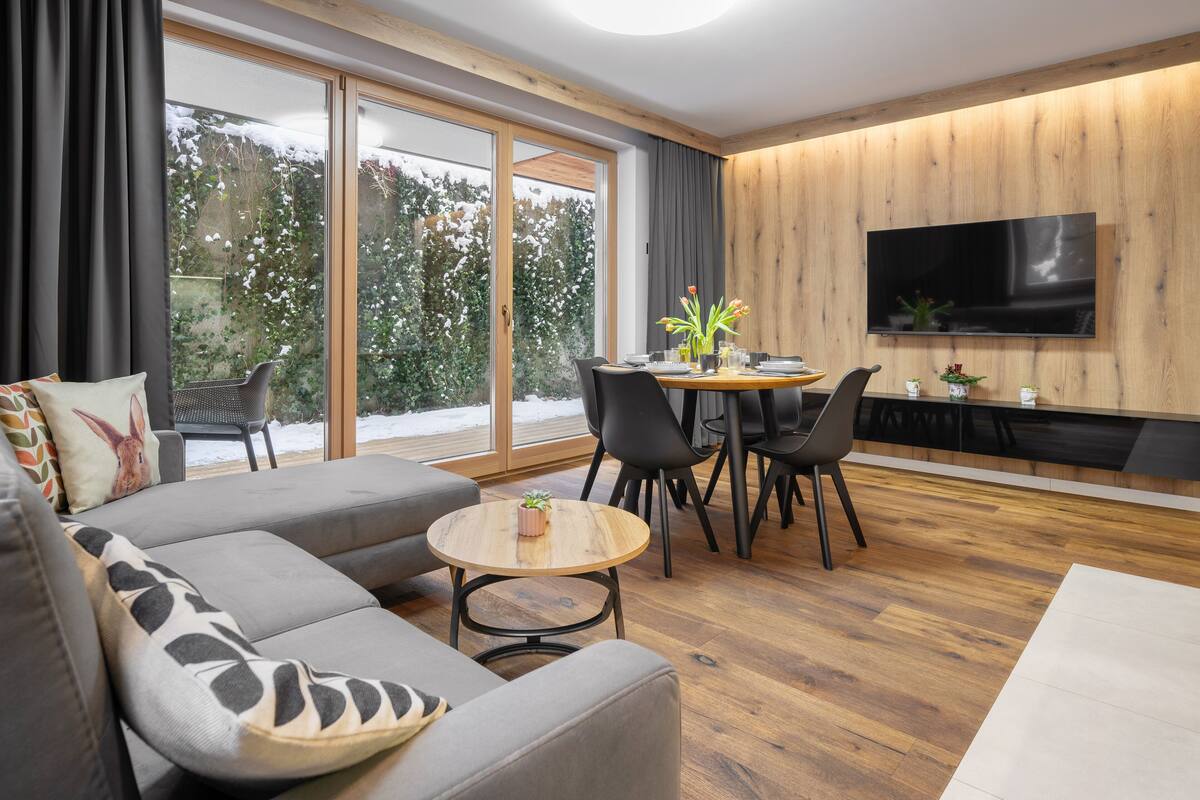 A modern living room with a grey sofa, a round coffee table, and a dining area with a wooden table and chairs.