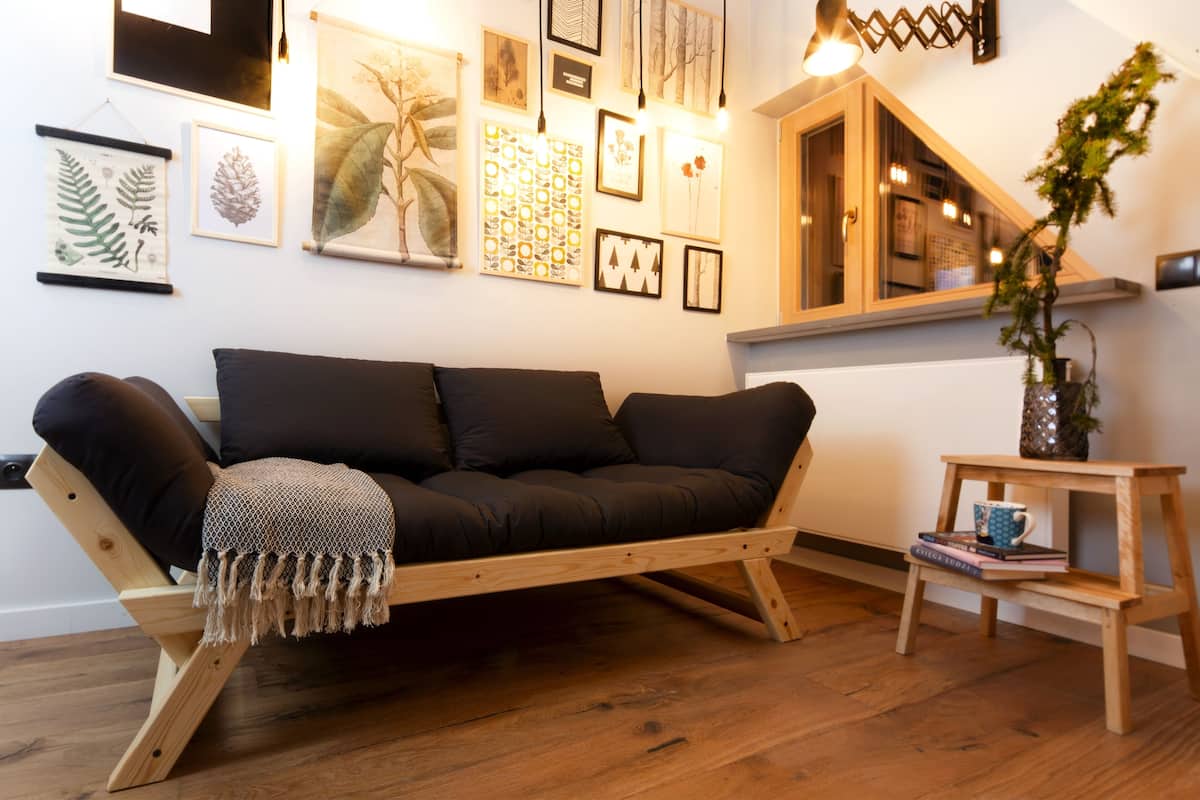 A modern living room with a wooden sofa, a small wooden side table, and a variety of framed botanical prints on the wall.