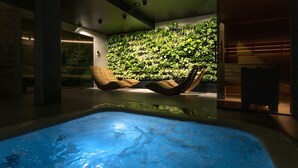A modern indoor pool area with a floating chair, a wall of green plants, and a glass partition. - Green Deer Premium (Zakopane)