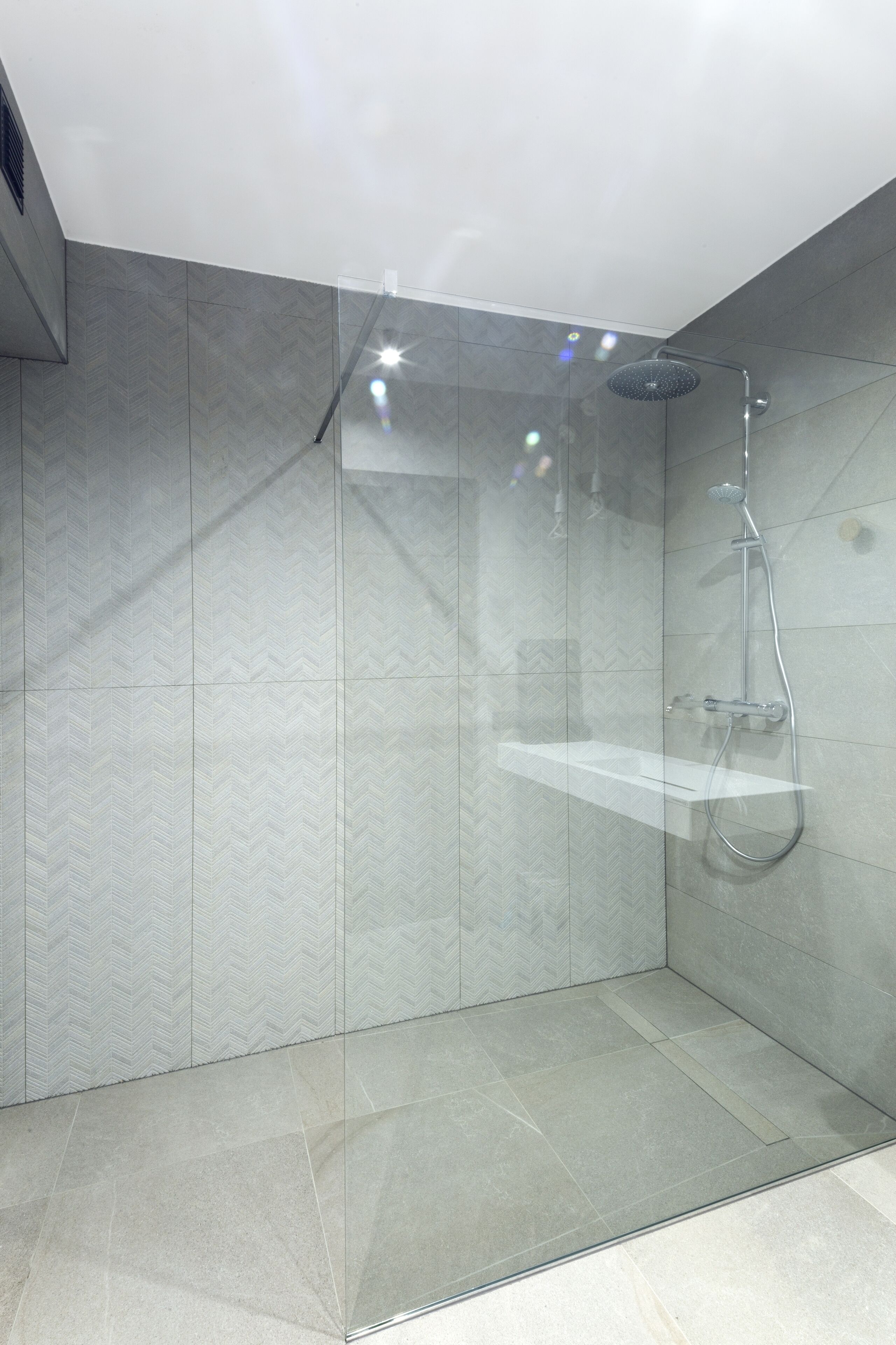 A modern shower with a glass door, a handheld showerhead, and a wall-mounted control panel.