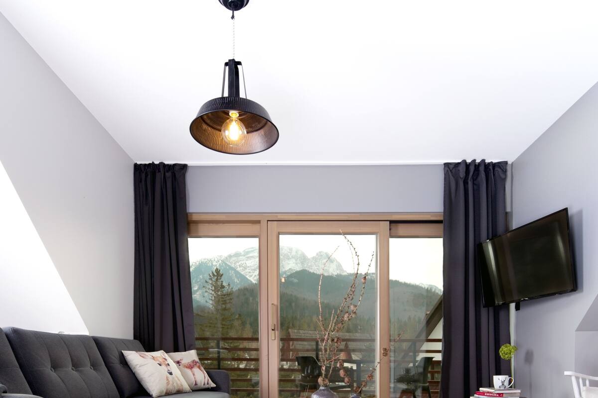 A modern living room with a grey sofa, wooden coffee table, and a large window with a mountain view.
