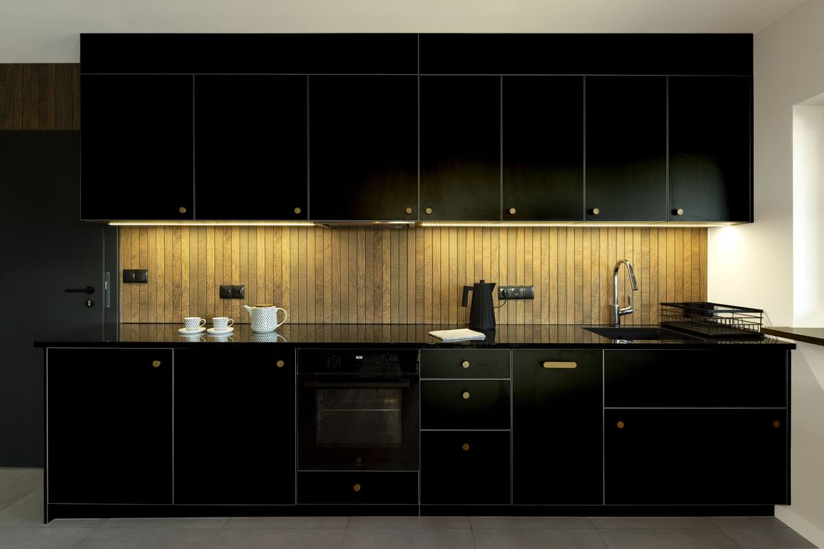 A modern kitchen with black cabinetry, a wooden backsplash, and a built-in oven.