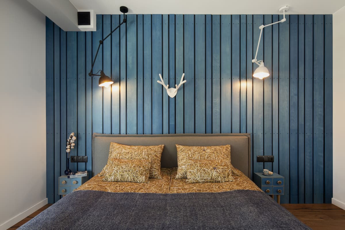 A bedroom with a bed, two nightstands, a wall-mounted deer head decoration, and two wall-mounted lamps.