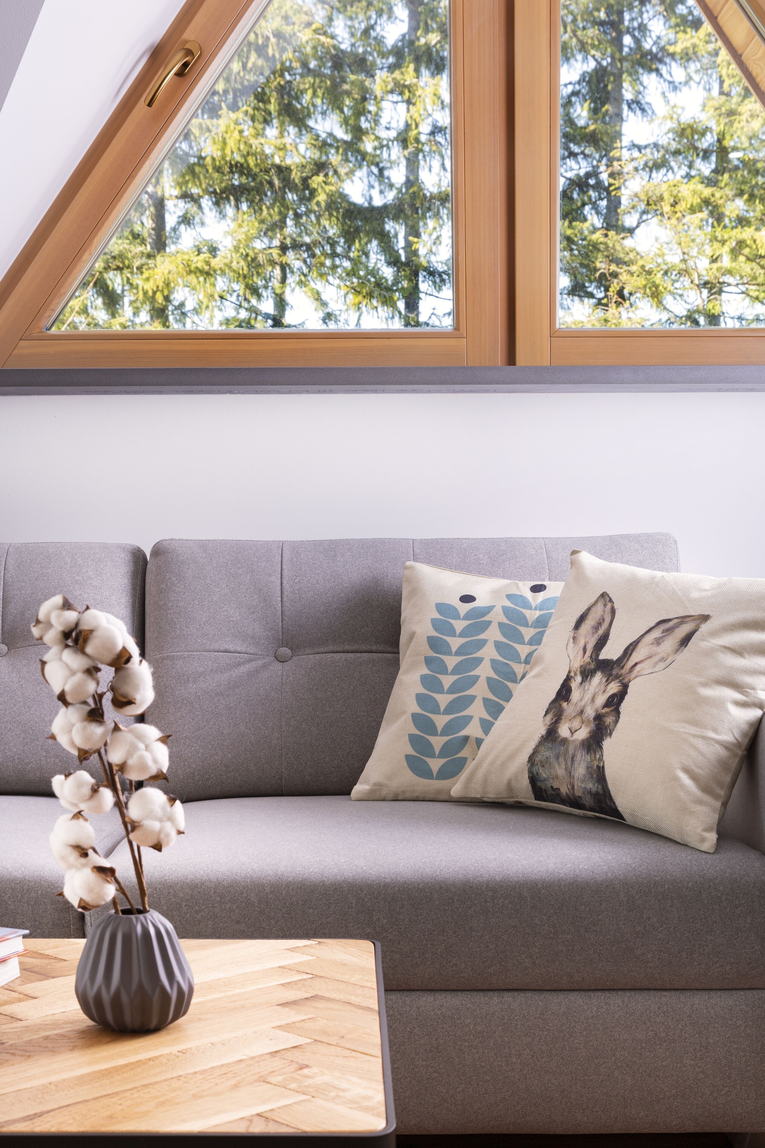 A modern living room with a grey sofa, a wooden coffee table, and a vase with cotton plants.